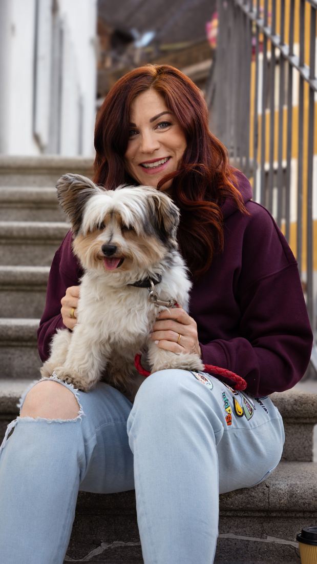 Nina Fleisch, Gründerin der TALAVY Social Suite, sitzt entspannt auf einer Treppe mit ihrem Hund Rio auf dem Schoß