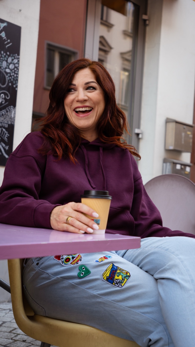 Nina Fleisch, Gründerin der TALAVY Social Suite, lacht bei einem Kaffee im Straßencafé